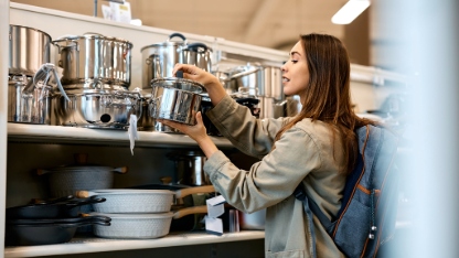 Young happy woman buying new cooking pot in the supermarket. Copy space.