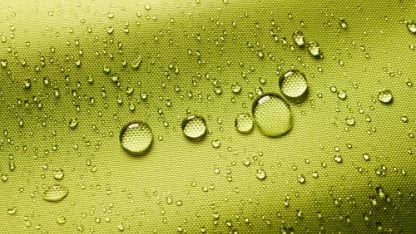 Top view closeup of green background with small round drops of water on textured waterproof impregnated fabric in light room