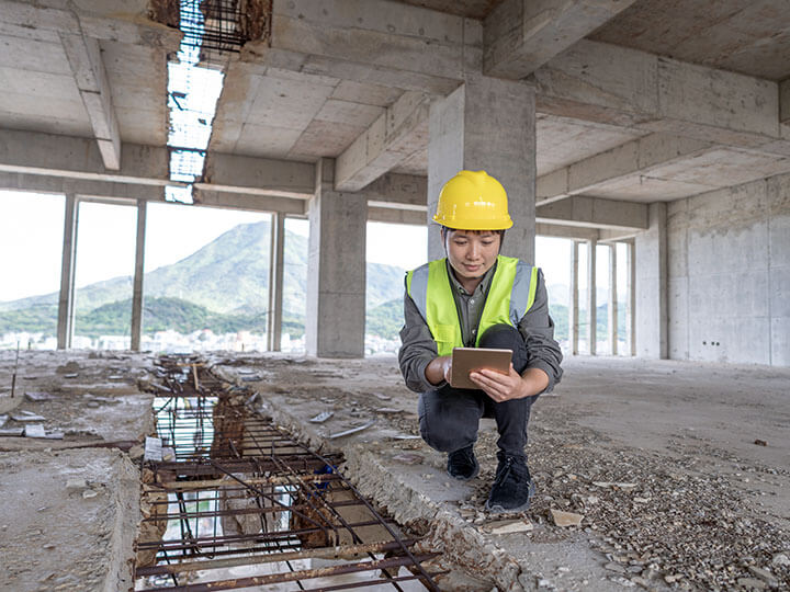 An engineer in a yellow hard hat and caution vest in the construction site working with a tablet to monitor a foundation crack