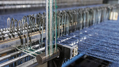 Closeup of indigo warp threads on a modern weaving machine showing precision denim manufacturing and automated textile production.