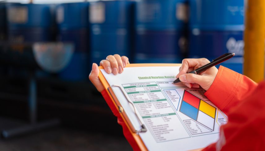 Chemical worker completing a Chemical Hazardous Materials identification form on a clipboard in an industrial facility.